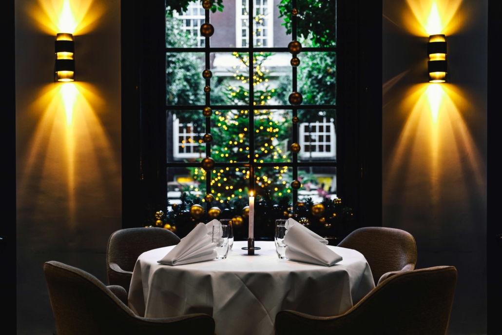 A set table during Christmas in 2 Michelin Star Restaurant Vinkeles, in luxury boutique hotel The Dylan Amsterdam. The serviettes are folded, glasses are polished and the candles are lit. View on the secluded garden.