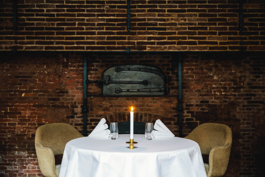 A set table in 2 Michelin Star Restaurant Vinkeles, in luxury boutique hotel The Dylan Amsterdam. The serviettes are folded, glasses are polished and the candles are lit. The background is from the old bakery from the 18th centruy.