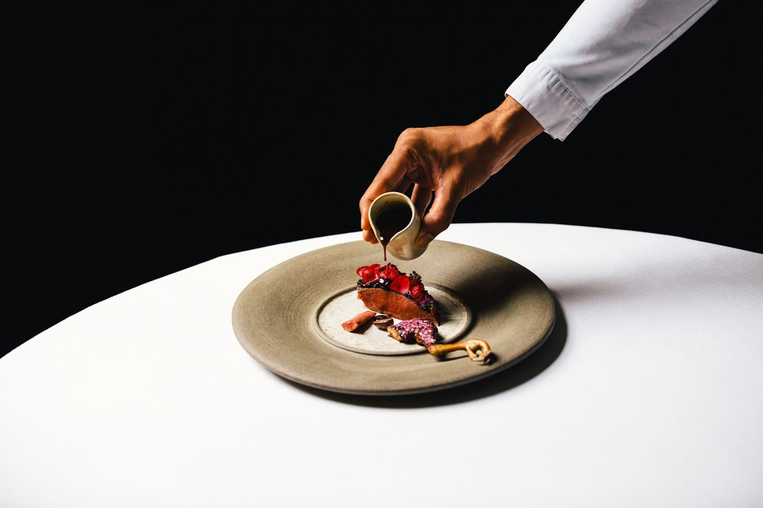 ANJOU PIGEON - Ponzu, red onion, sour cherry, rose, Cusco Chunco 100%. A dish at 2 Michelin star Restaurant Vinkeles, in luxury boutique hotel The Dylan Amsterdam. Executive Chef Jurgen van der Zalm pouring the sauce on the dish.